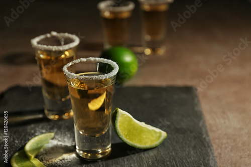 Gold tequila shots with lime slices and salt on grey board
