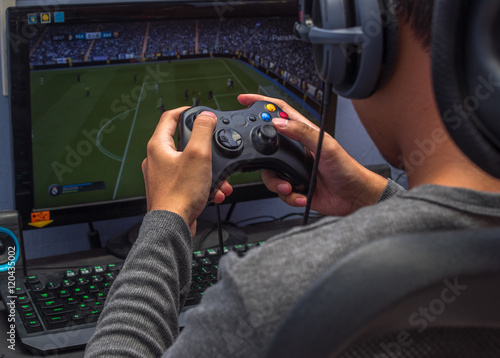 Back view of young gamer playing video game wearing headphone using his controller. photo