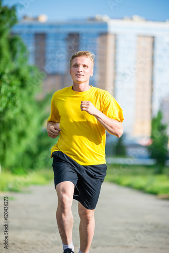 Running man jogging in city street park at beautiful summer day. Sport fitness model caucasian ethnicity training outdoor.