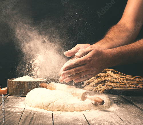 Tableau sur toile Man preparing bread dough on wooden table in a bakery