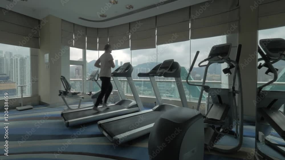 Clip of young blond woman going on the treadmill in fitness centre looking at window with modern building cityscape and then begin to run. Hong Kong, China Clip of young blond woman going on the treadmill in fitness centre looking at window with modern building cityscape and then begin to run. Hong Kong, China