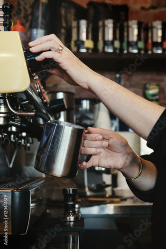 Woman barista making espresso coffee and frothing milk
