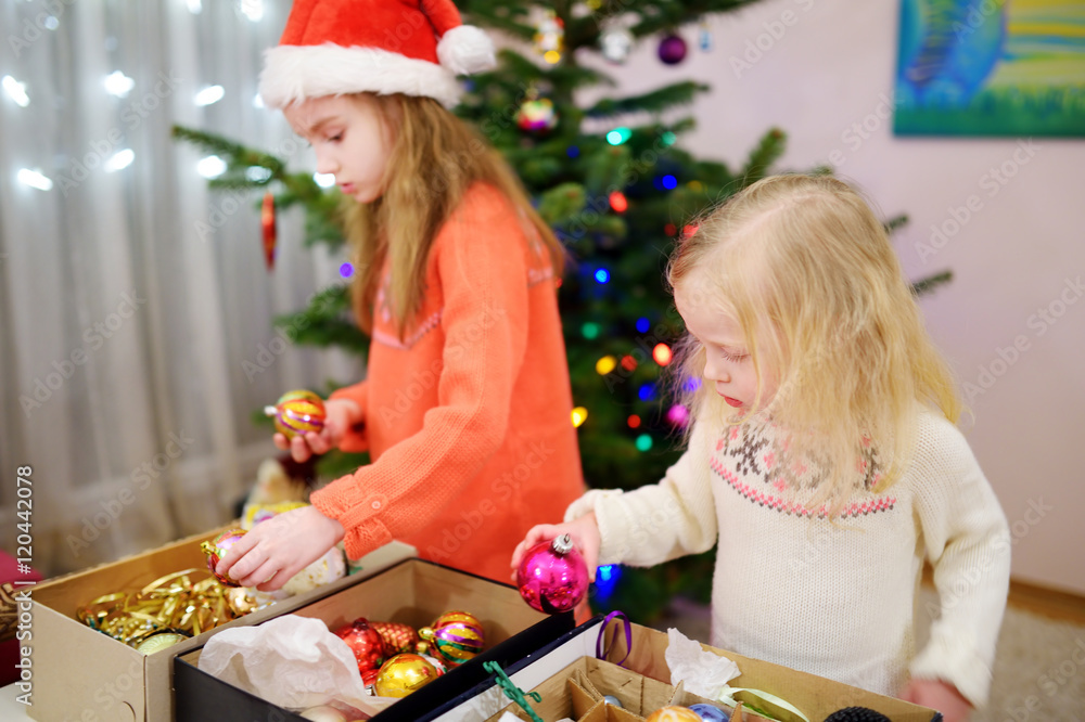 Two adorable little sisters decorating a Christmas tree