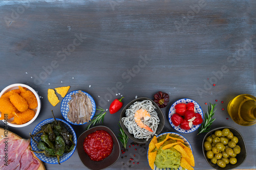 Table with spanish tapas - anchovies with peppers padron, jamon, croquetes, guacamole and olives, border with copy space, picnic table