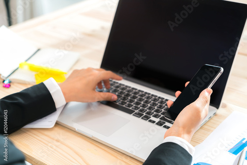 Closeup of business woman hand touch phone over laptop keyboard
