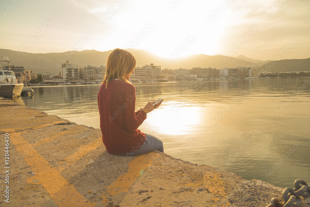 Girl using cellphone near the bay in sunrise / sunset.