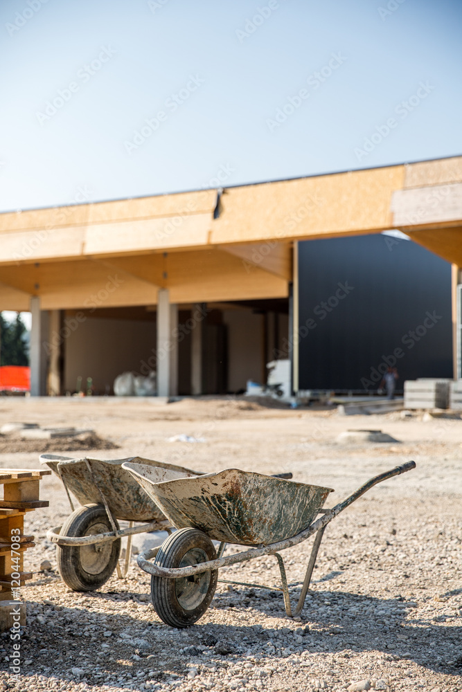 Two wheelbarrows in front of a construction site for small business premises. Property construction, small scale enterprise, expanding property concept. Two wheelbarrows in front of a construction site for small business premises. Property construction, small scale enterprise, expanding property concept.