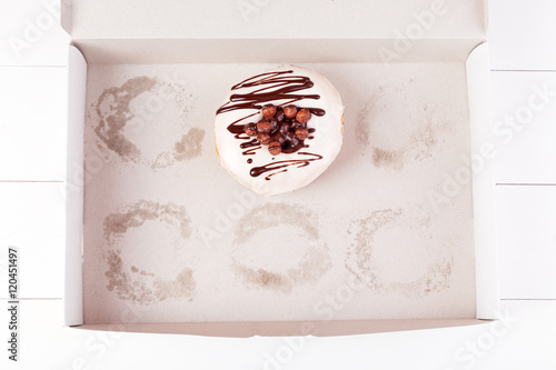 One delicious donut with sprinkles in a empty box on a white wooden background. Top view with copyspace