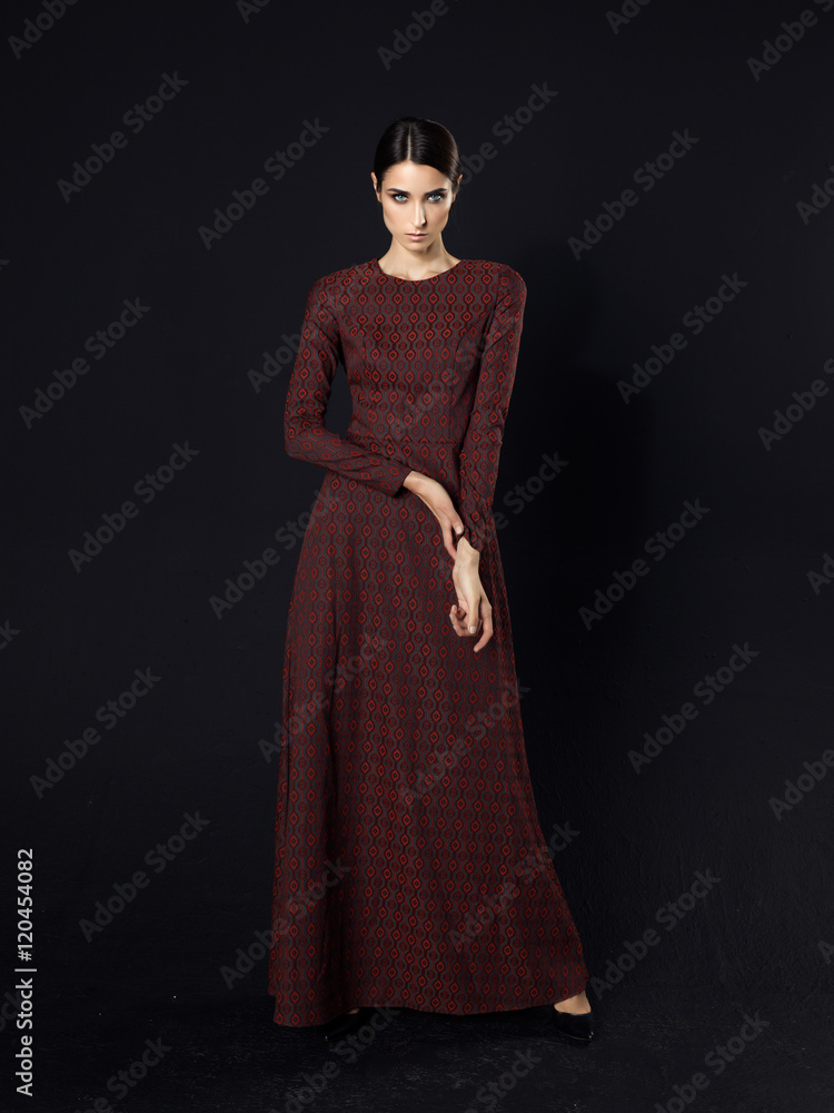 Fashion model wearing long maroon dress on black background Stock Photo