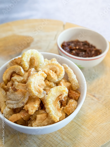 Pork snack, pork rind in bowl with thai chili sauce on wood block