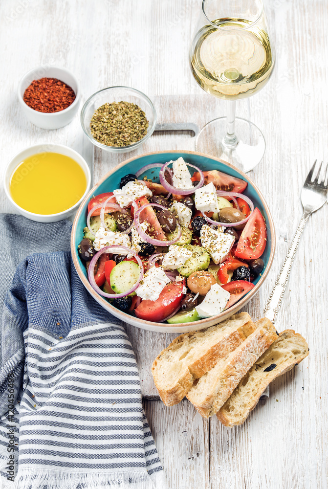 Greek salad with olive oil, bread, oregano, pepper and glass of white wine over old white painted wooden board, top view, selective focus, vertical composition Greek salad with olive oil, bread, oregano, pepper and glass of white wine over old white painted wooden board, top view, selective focus, vertical composition