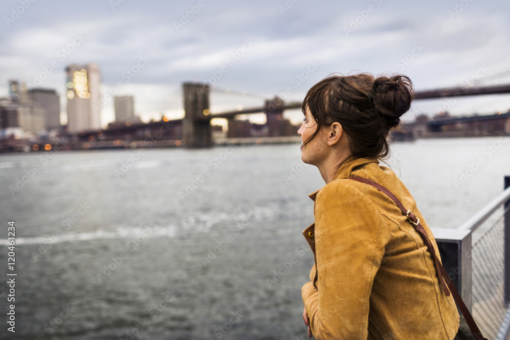 Woman looking at East River at dusk, Brooklyn Bridge in background