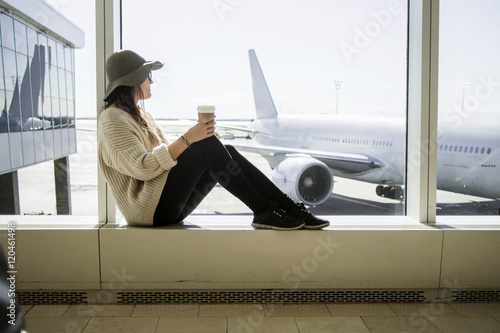 Young woman holding disposable coffee cup and waiting at airport photo