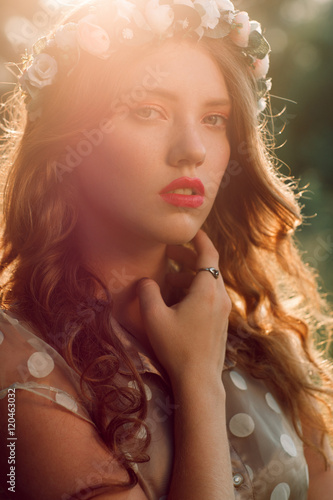 Beautiful girl in wreath touching her neck, sunset light and forest background. Healthcare, alternative medicine, medicinal herbs, witch, wise woman concept