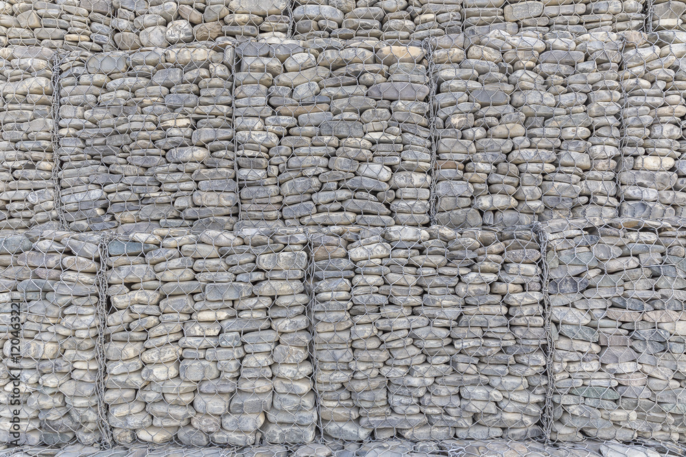 Fototapeta premium The wall of river stones packed in a metal grid