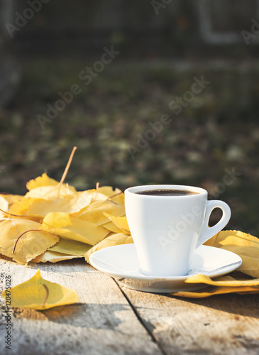 cup of espresso coffee on an autumn nature on the old wooden table with a yellow listh photo