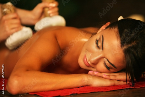 Young woman lying on wooden spa bed. Poultice hot herbal massage in spa salon.