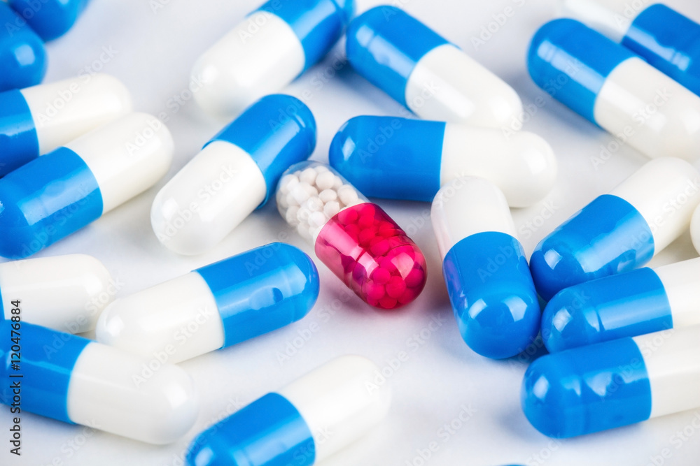 Blue capsules around pink transparent capsule on white Blue capsules around pink transparent capsule on white