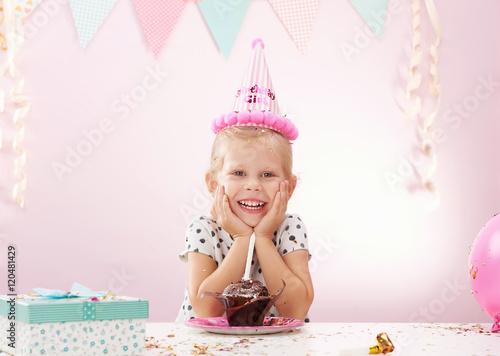 Joyful little girl having birthday party at home. Cute kid with gift box and cupcake in the room.