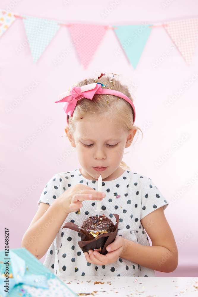 Beautiful 4 years girl celebrating her birthday at home. Cute child holding chocolate muffin with candle at the table. Beautiful 4 years girl celebrating her birthday at home. Cute child holding chocolate muffin with candle at the table.