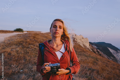 portrait of attractive young blonde woman tourist standing with an retro camera in hands on a background of mountain peaks, cliffs and the sea © skvalval