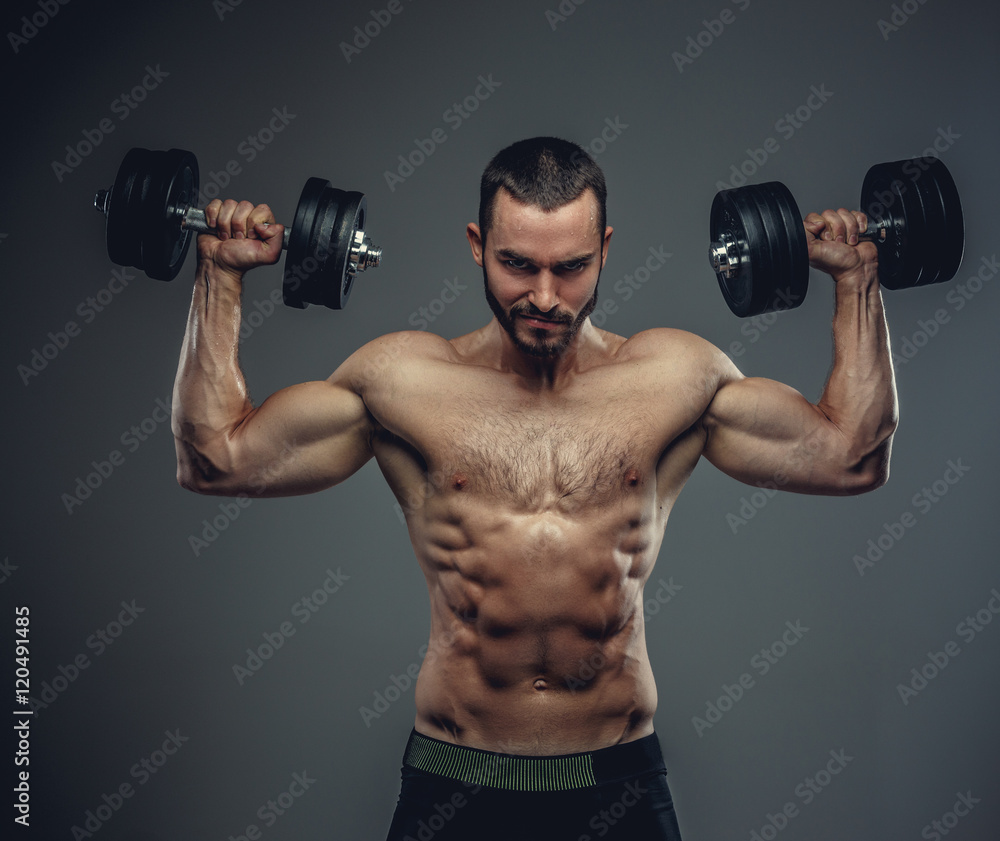 A man holds dumbbells with arms up on grey background.