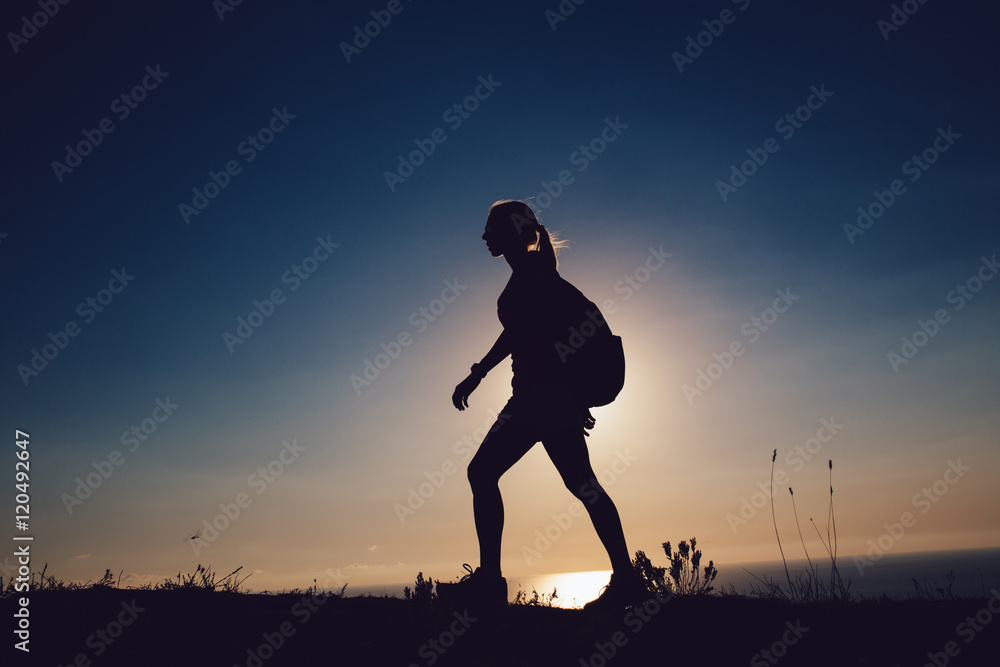 silhouette Young woman tourist with backpack goes outdoor on the background on sunset sky