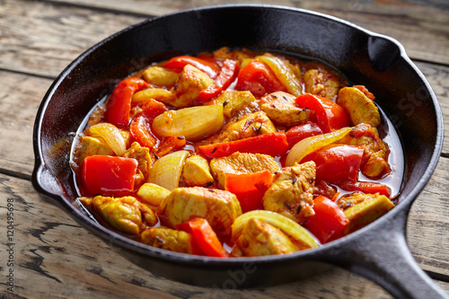 Chicken jalfrezi healthy traditional Indian culture curry spicy fried meat with chilli and vegetables, tomatoes, pepper, onion, asian food in cast iron pan on vintage table background