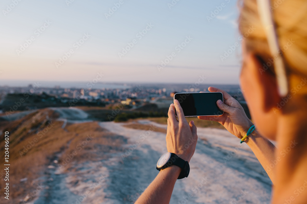 Cropped shot view of woman's hands holding modern mobile phone with blank space screen for your text message or information content. Blurred view hill, city and sea on a background.