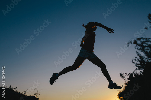 silhouette Young woman tourist with backpack jumping through the gap between hill. Woman jumping between two mountains