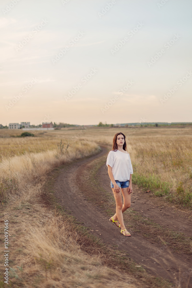 Young girl with long brown hair walking along the road in field