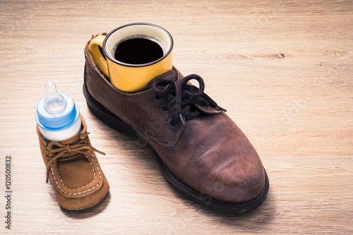 coffee cup in father shoes and milk bottle in child shoes, love and bound concept