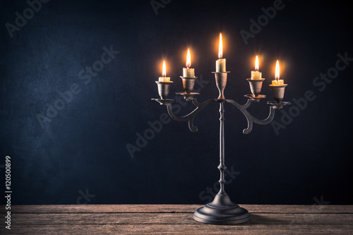 handicraft candelabrum with burning candles on old wooden table against art dark background