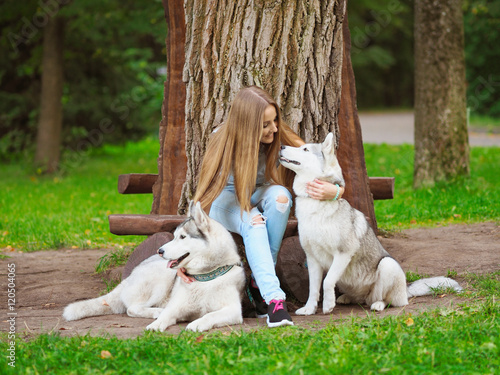Attractive young woman sits on a bench with two funny siberian husky dogs