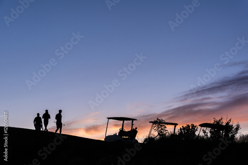 golfers and golf carts silhouetted by sunset