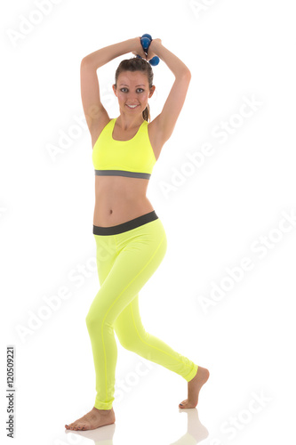 A brunette beautyful barefeet smiling young woman in bright yellow sports bra and trousers doing exercises for body with dumbbells in hands above the head