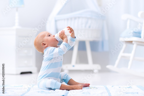 Baby boy drinking milk in sunny nursery photo