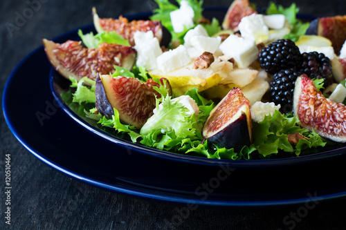 Salad with pears, lettuce, figs, walnuts, goat cheese, walnuts and honey on black background
