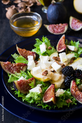 Salad with pears, lettuce, figs, walnuts, goat cheese, walnuts and honey on black background