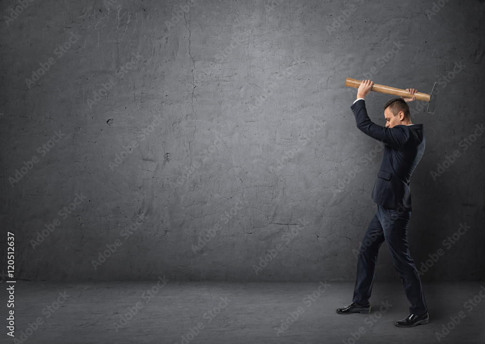 Side view of businessman with big hammer in his arms destroying something Side view of businessman with big hammer in his arms destroying something