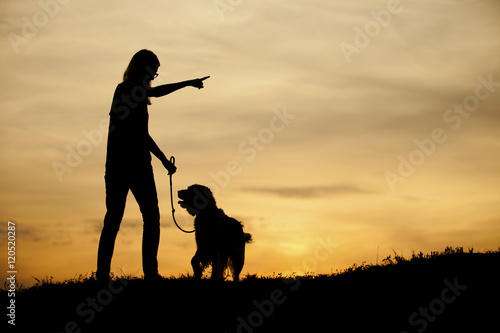 Silhouette of girl and her dog with beautiful sunset background.