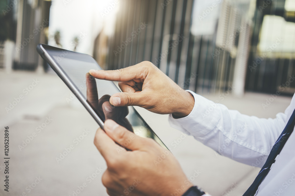 Close-up of male hands typing text message on digital tablet, businessman holding and using modern tablet pc outside, focus on hands, office buildings in the background Close-up of male hands typing text message on digital tablet, businessman holding and using modern tablet pc outside, focus on hands, office buildings in the background