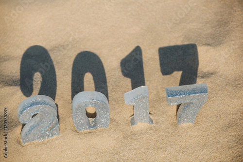 Four New Year's figures are in the sand on the beach or seaside, cast a large shadow on the ground. New Year Celebration and Christmas in the ocean, the sea. Traveling.
