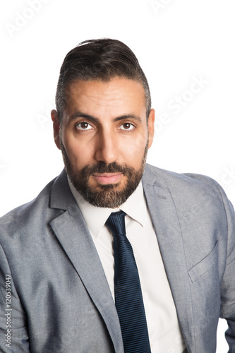 A mature businessman in his 40s wearing a grey suit with a blue tie, sitting down on a chair looking at camera. White background.