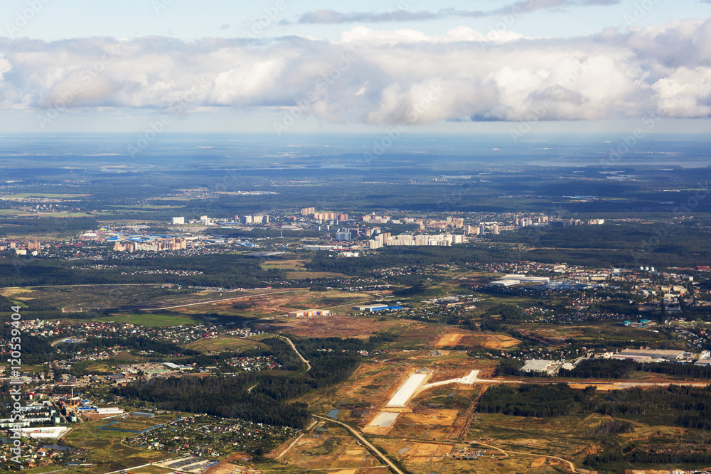 Small town near the forest in Russia. Aerial view of thick clouds and their shadows over the land, the landscape.