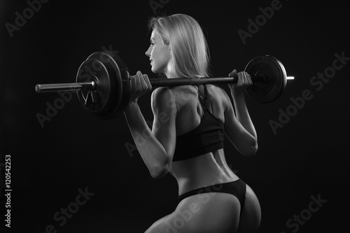 Girl with a barbell on black background