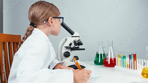 Portrait in profile young chemist school girl 7-8 years using microscope and writing in her notebook. Isolated on white