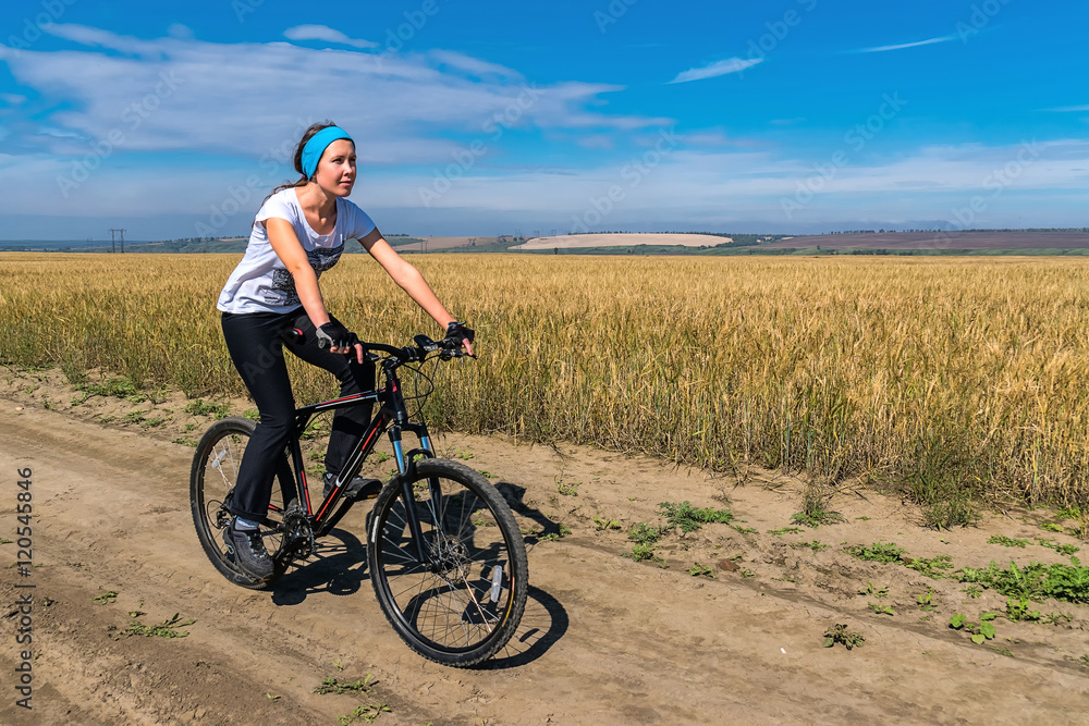 girl rides bicycle on the road in a field