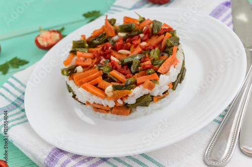 Rice and fried vegetables (asparagus beans, carrots) - vegan diet garnish. Decorated layers of salad on a white plate.