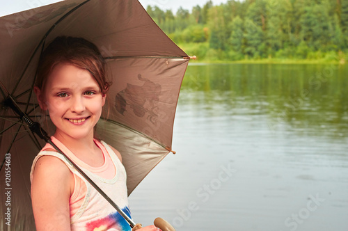 Little girl with an umbrella in cloudy day near the lake
